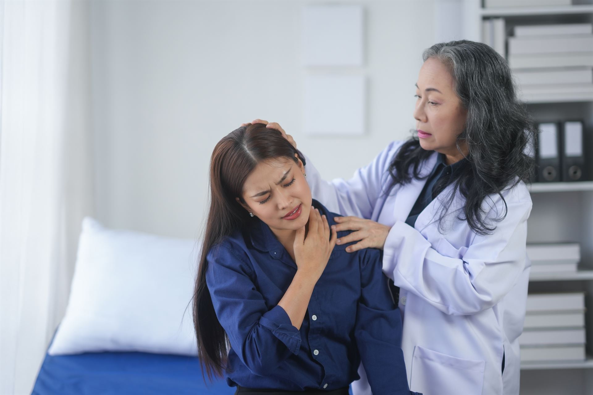 Doctor examining a patient's neck pain in a medical office. The patient appears to be in discomfort while receiving professional care. Mass Image Compressor Compressed this image.