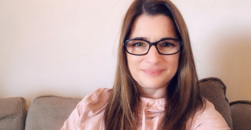 Beth smiling in a selfie from her home sofa.