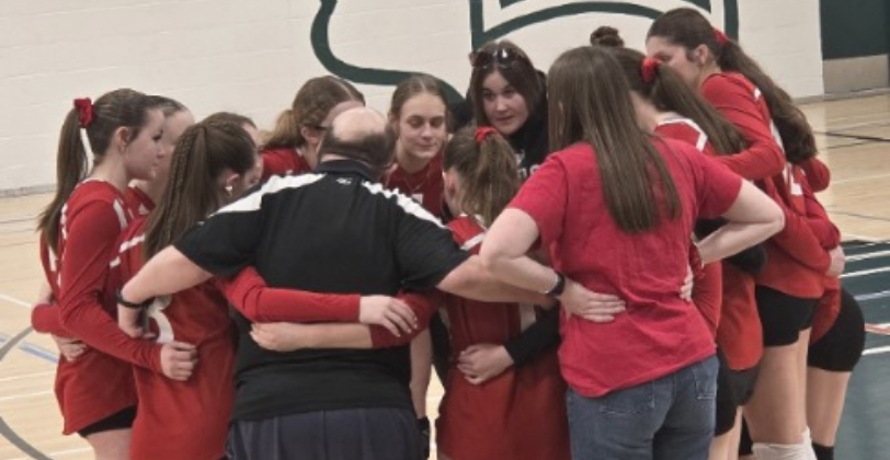 Ed is in a huddle with a team of younger students in a school gymnasium.